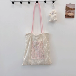 Detailed close-up of a lace canvas tote bag with a floral pocket and plush charm accessory
