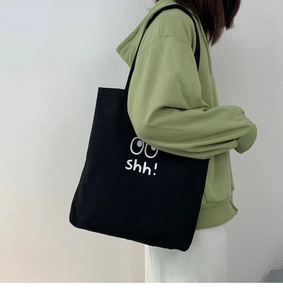 Vista lateral del bolso tote de lona negra con texto blanco usado por una modelo