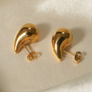 Polished 18k gold-plated teardrop stud earrings placed on smooth beige silk fabric