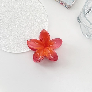 Detail view of a vibrant red and orange gradient flower hair claw on a white desk