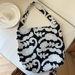 Detail of black canvas bag featuring white paisley embroidery and simple wish label