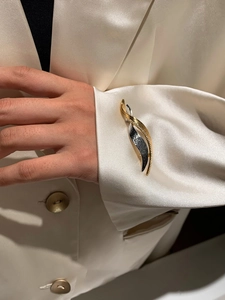 Detail of a sparkling zircon twisted leaf brooch on a white satin blazer sleeve