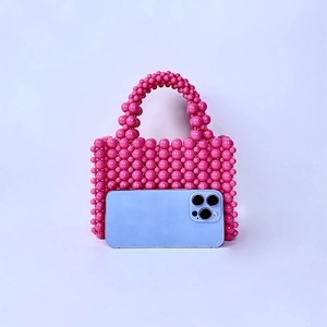 Pink beaded handbag handcrafted with pearls shown next to a smartphone for size reference