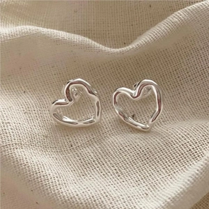 Macro shot of silver hollow heart earrings on beige textured linen fabric background