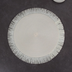 Macro shot of off-white circular woven placemat with fringed edges on stone surface