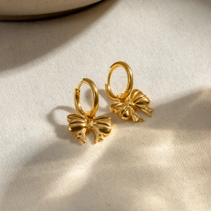 Fashionable 18k gold stainless steel bow earrings on a beige linen surface