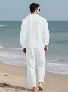 Vue arrière d'un homme en ensemble blanc coton-lin marchant sur une plage de sable