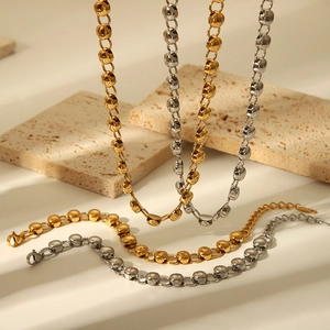 Polished gold and silver bead chain necklaces set on textured stone with warm shadows