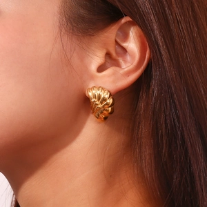 Detailed view of model wearing gold-plated wave-textured shell earrings with golden finish