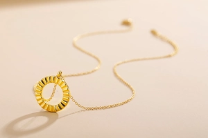 Macro detail of a golden pleated circular pendant necklace with refined metal texture