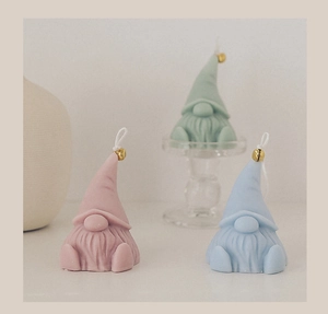 Three colorful Christmas gnome candles with golden bells and cotton wicks on display