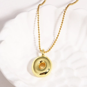 Detailed view of a gold-plated bubble letter necklace on a white textured shell background