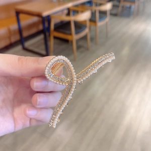 Detailed close-up of golden infinity hair claw clip with faux pearls and rhinestones