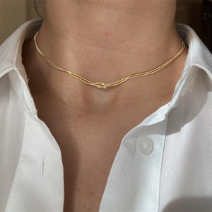 Close-up of gold plated snake chain necklace with a centered knot design on a model's neck