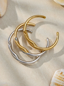 Dettaglio di bracciali a polsino intrecciati lucidi in oro e argento su fondo sabbioso