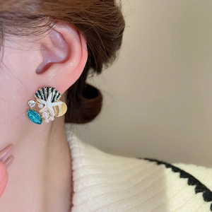 Detail of marine earrings with blue shell, starfish, and pearls worn by a model