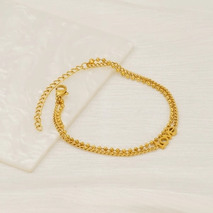 Detail of gold double-layered bracelet with beads and flat link chain featuring LOVE charm