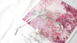 Detail of silver grey organza jewelry pouch with bow, holding pearl and gold rings