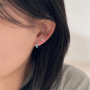 Detail of 925 sterling silver hoop earrings with blue square gems on a model's ear