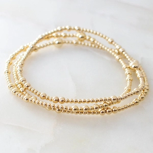 Three-piece set of polished gold bead stretch bracelets on a white marble background