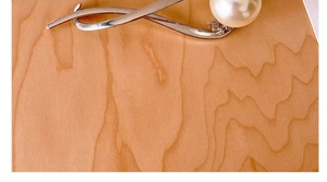 Close-up of a silver alloy hair clip featuring a white pearl on a natural wood surface