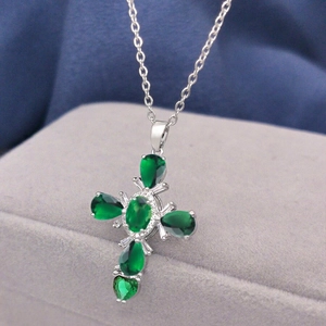 Luxurious silver cross necklace featuring green zircon stones on a gray jewelry box