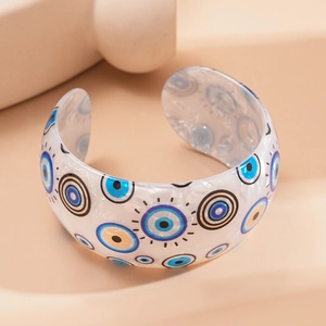 Detailed view of white acrylic cuff bracelet with blue and yellow evil eye patterns