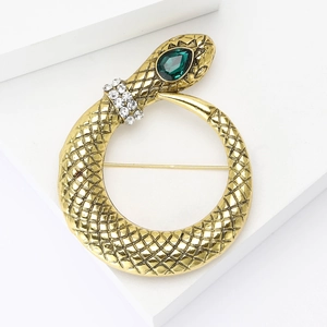 Macro shot of gold snake brooch showing detailed scales and a green teardrop gemstone