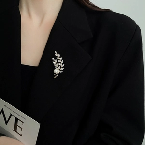 Detail of wheat stalk brooch with sparkling zircons and white pearl on a black suit blazer