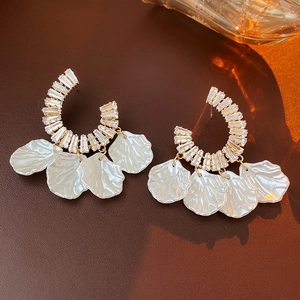 Detail of C-shaped gold-plated earrings featuring clear zircons and white flower petals
