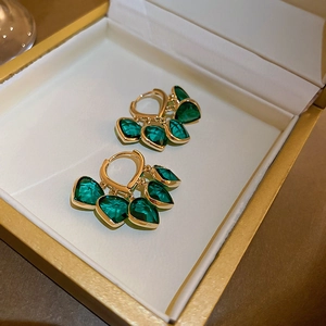 Close-up of gold earrings with green teardrop stones in a white jewelry box