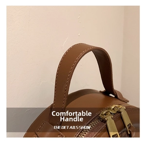 Detail der braunen Ledertasche mit verstärktem Griff und goldenen Doppelreißverschlüssen