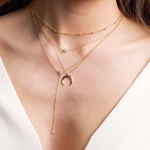Dettaglio della collana a strati con perline dorate e collana a Y con ciondolo a mezzaluna