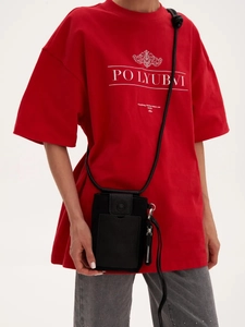 Close-up of a black synthetic leather mini crossbody phone bag with front pocket on red shirt