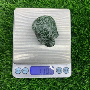Close-up of a 5cm carved green gemstone skull being weighed on a digital scale