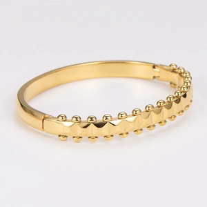 Gold stainless steel wavy studded bracelet with industrial design on white background
