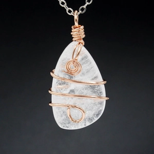 Macro shot of handmade wire wrapped clear crystal pendant with rose gold spirals