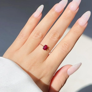 Macro detail of red oval zircon ring with rose gold chain band worn on finger