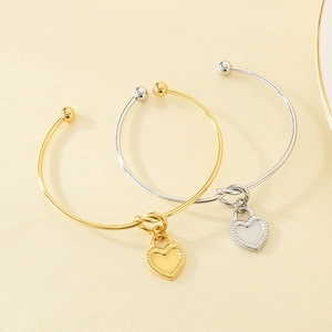 Polished gold and silver knotted C-shaped bracelets with heart charms on textured surface