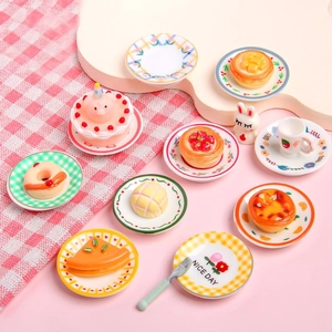 Miniature resin food play set with cakes, donuts, and floral plates on pink background