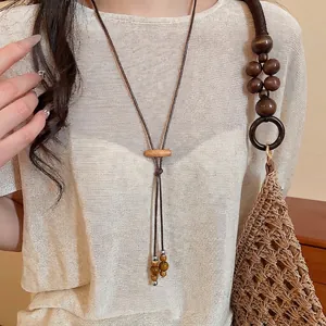 Bohemian wax rope necklace with wooden beads and ceramic tassel on a beige knit sweater