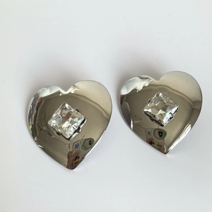 Macro detail of silver heart earrings featuring a centered square sparkling crystal