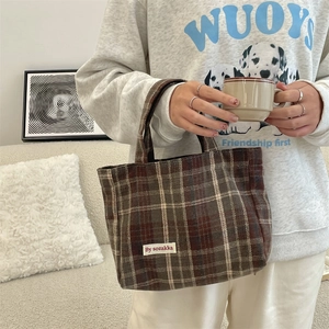 Detail view of the brown plaid tote bag featuring the woven brand label and fabric texture