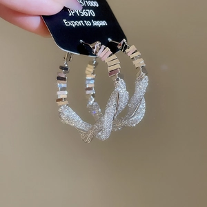 Detail of twisted 925 silver hoop earring with glittering mesh texture and polished accents