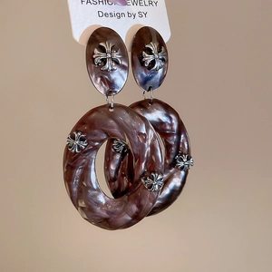 Macro detail of acrylic hoop earrings with marble texture and silver metal cross charms