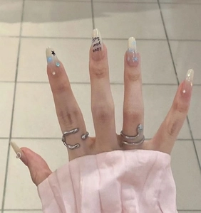Detail of almond nails with blue star design and silver rings on hand with cold tile background