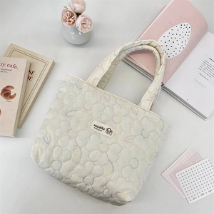 Close-up of quilted cream canvas tote bag with colorful floral embroidery and brand tag