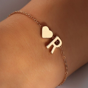 Gros plan détaillé d'un pendentif en cœur doré et d'une lettre R sur un bracelet fin