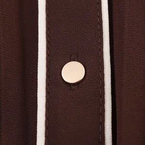 Detailed macro view of dark coffee chiffon fabric with white trim and a gold metal button