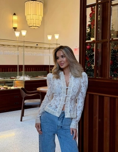Détail de la blouse blanche en dentelle à manches longues avec motifs floraux et lacets